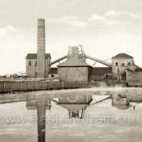 South Hetton Colliery c1930. This picture shows the surface facilities, including at least one Winding House, at a stage well before the redevelopment of the mid-1950s.  It is taken from the Easington to Wardley road (later A182), across the pond which produced thousands of froglets every spring before it was filled in and converted into a car park.  The camera is pointing approximately north-eastward.   Caption by Sheldon Clark